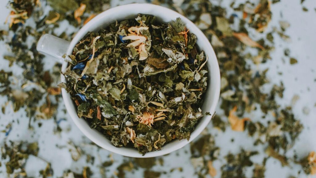 Overhead shot of a cup with a blend of dried herbal tea leaves and flowers.