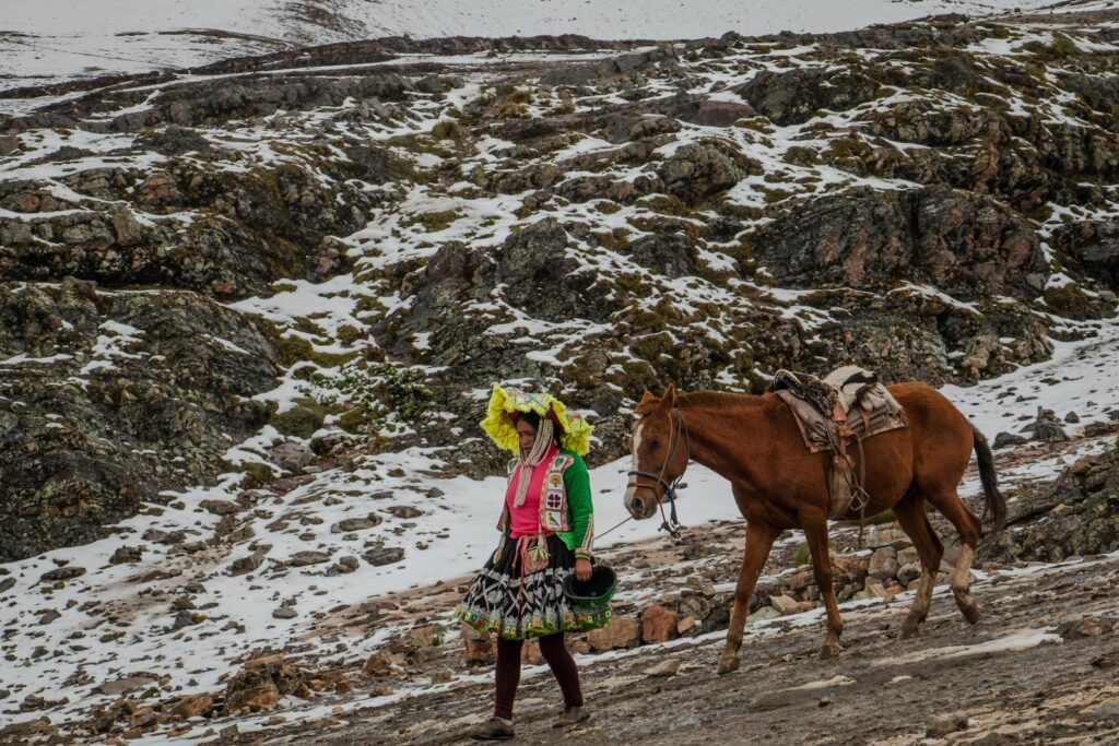 Andean woman in traditional attire walks beside a horse