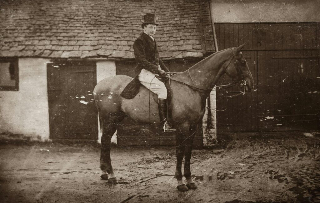 A sepia-toned classic portrait of a man riding a horse in a rural setting.