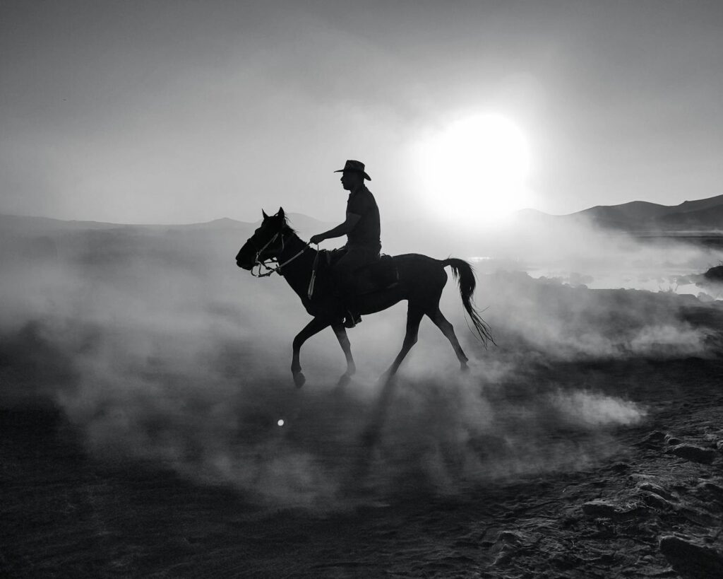A cowboy riding a horse through dust in Hürmetci, Kayseri, Türkiye at sunset.