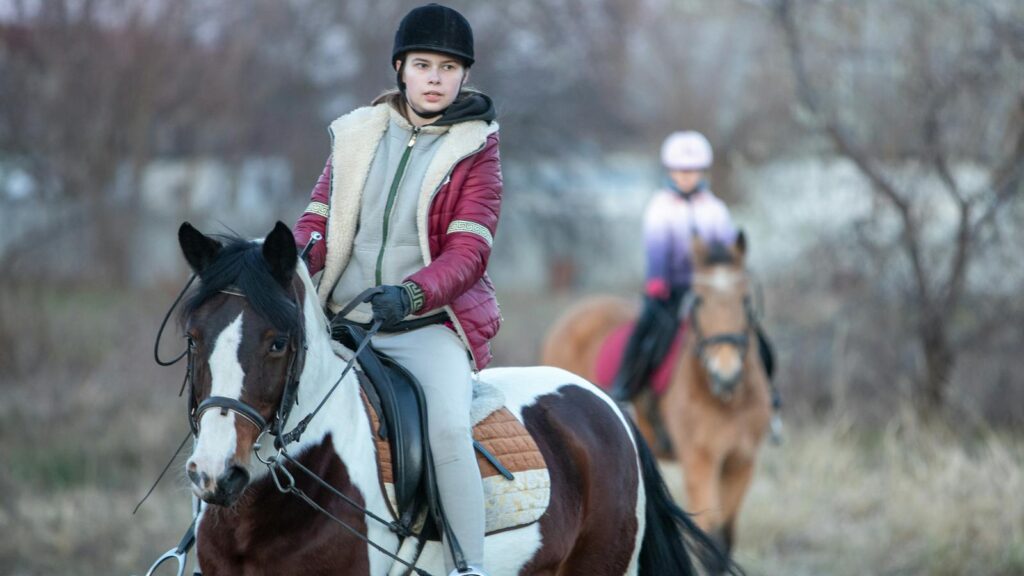 A teenager riding a horse in a rural setting, showcasing equestrian skills.