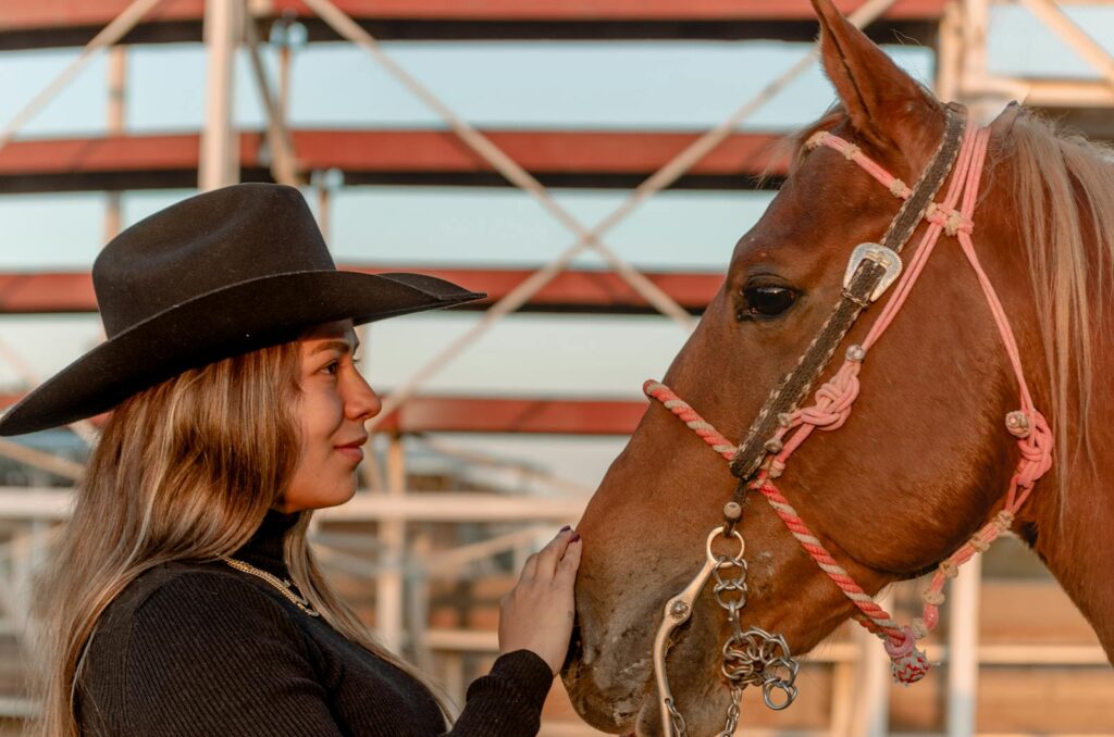A young woman in a cowboy hat shares a touching moment with a brown horse outdoors.