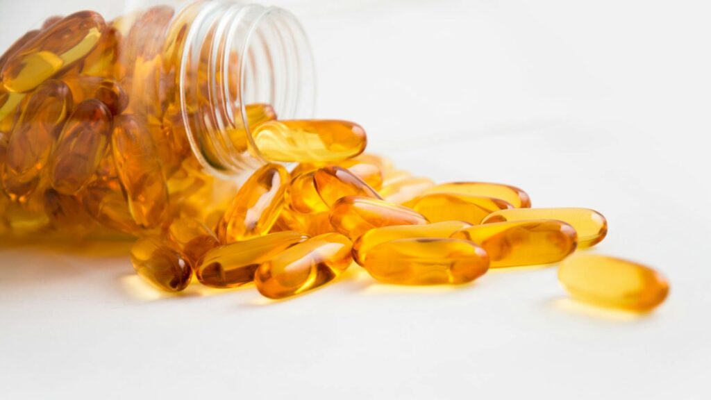 Close-up of fish oil capsules spilling from a bottle on white background.