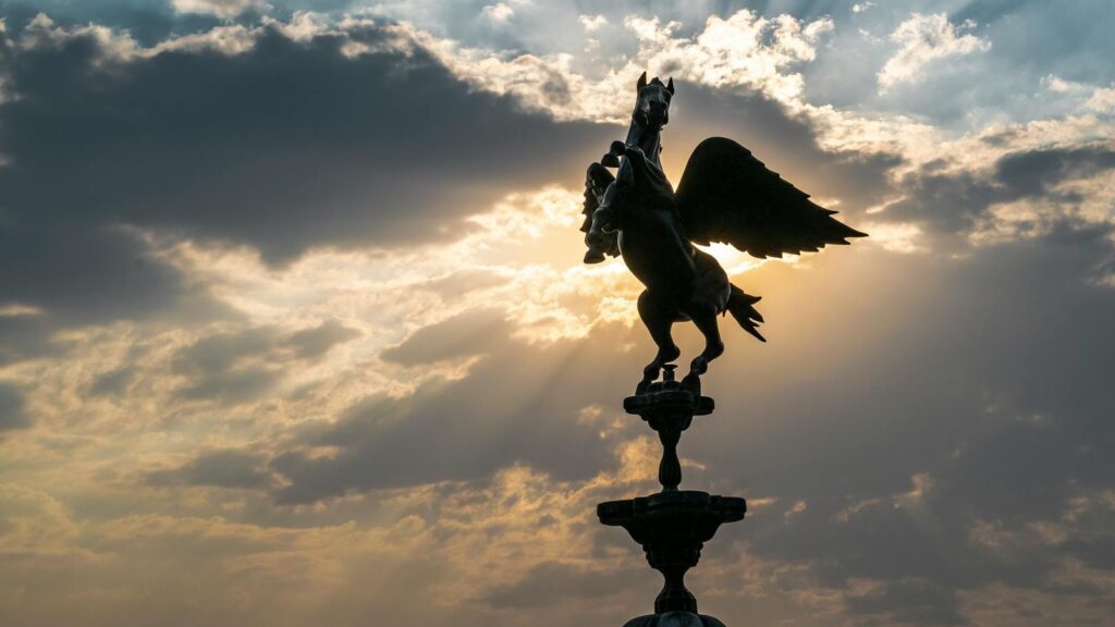 A stunning silhouette of a Pegasus sculpture against a dramatic sunset sky with sun rays.