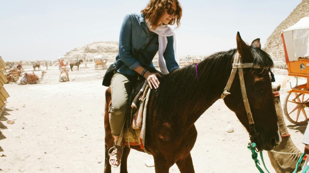 A woman riding a horse near the iconic pyramids in a desert setting.