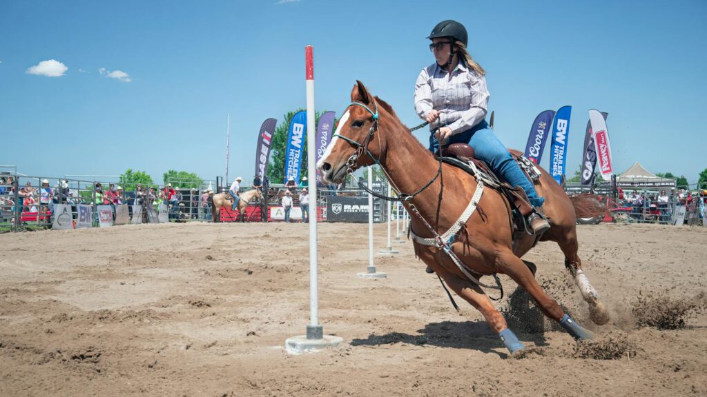 Woman in a rodeo event on horseback navigating poles outdoors.