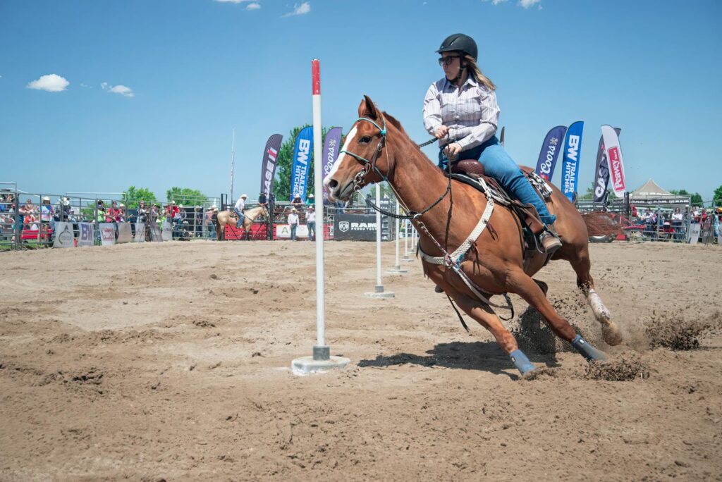 Woman in a rodeo event on horseback navigating poles outdoors.