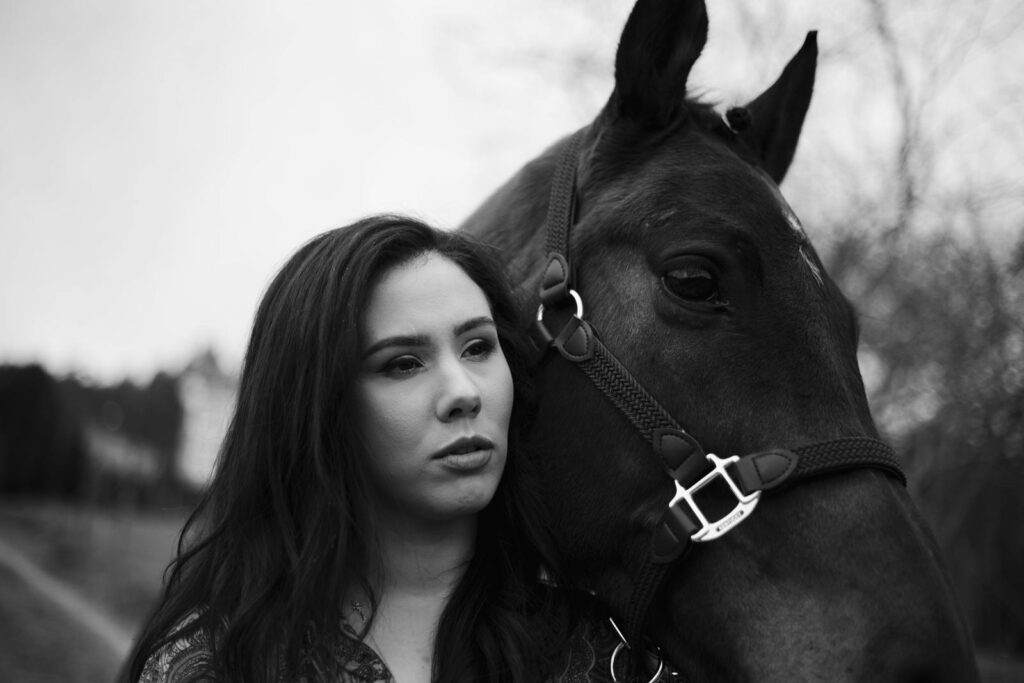 Black and white image of a woman beside a horse, outdoors, emphasizing connection.