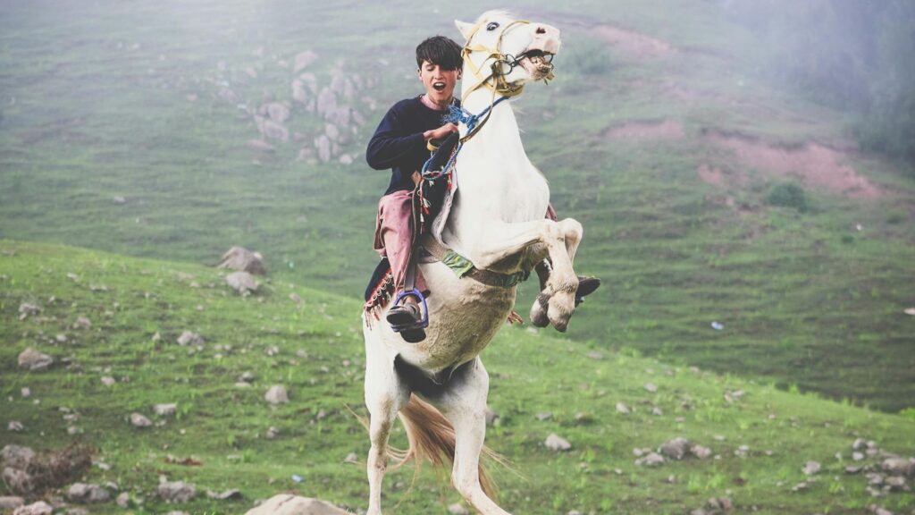 A young man rides a rearing horse amidst the lush green hills of Naran, Pakistan.
