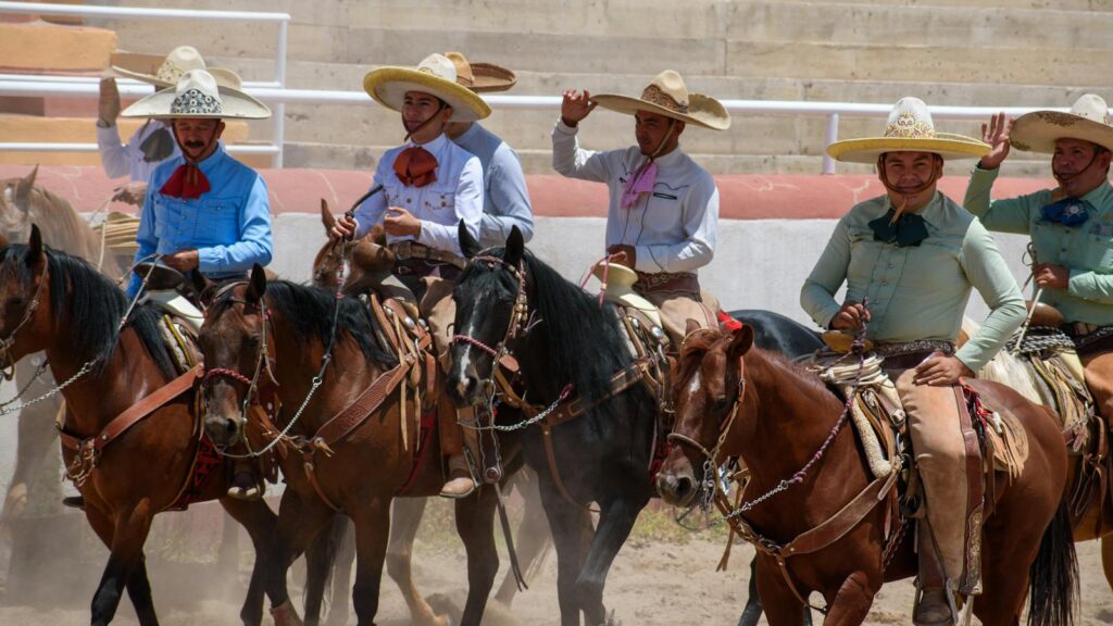 A group of Mexican charro cowboys in traditional attire riding horses in a rodeo arena, showcasing cultural heritage.