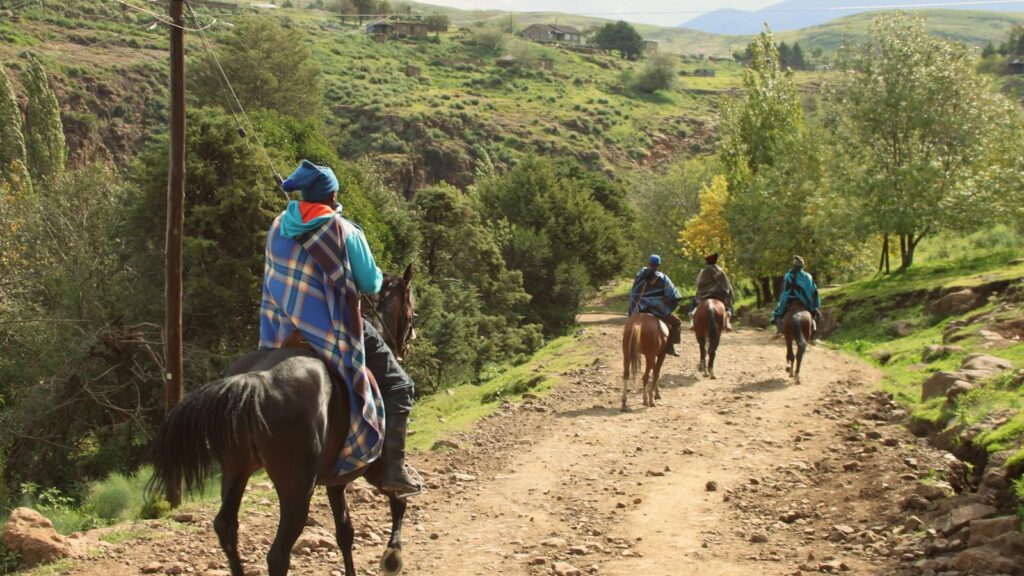 Horse riders on a scenic dirt trail in Semonkong, Maseru, Lesotho, surrounded by lush greenery.
