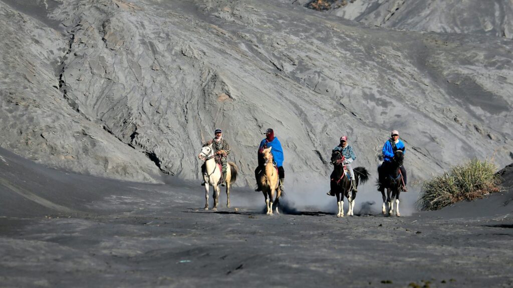 Adventurers on horseback traverse a dramatic volcanic landscape in daylight.