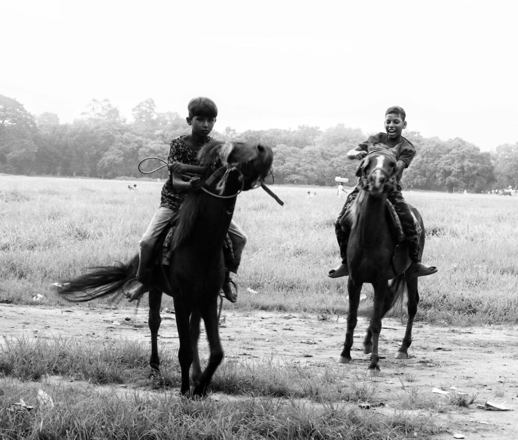 Two boys riding horses in an open field, captured in black and white.