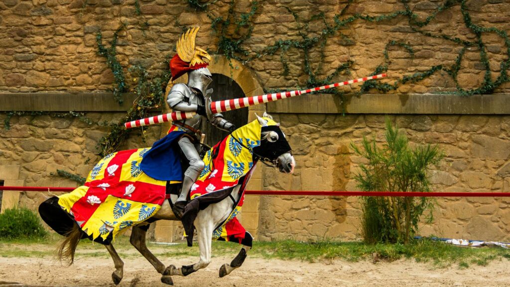 A medieval knight in full armor jousting on a decorated horse against a rustic stone wall backdrop.