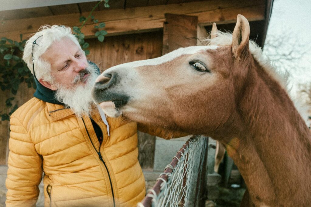 Elderly man in a yellow jacket interacts warmly with his horse