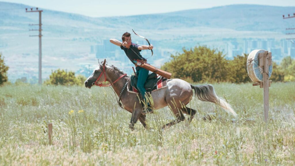 A horseback archer practicing in a lush green field in Konya, Türkiye.