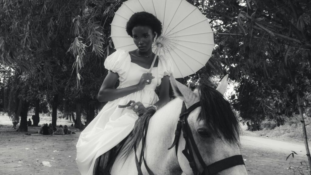 Elegant woman in vintage dress riding a horse, holding a parasol, black and white image.