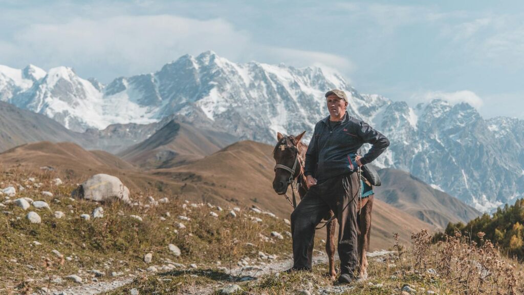 A man stands with his horse against a stunning snowy mountain backdrop.