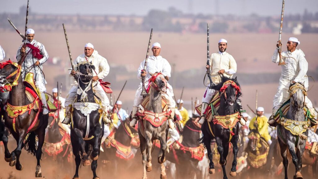 Moroccan Fantasia horsemen in traditional attire, charging across the field.