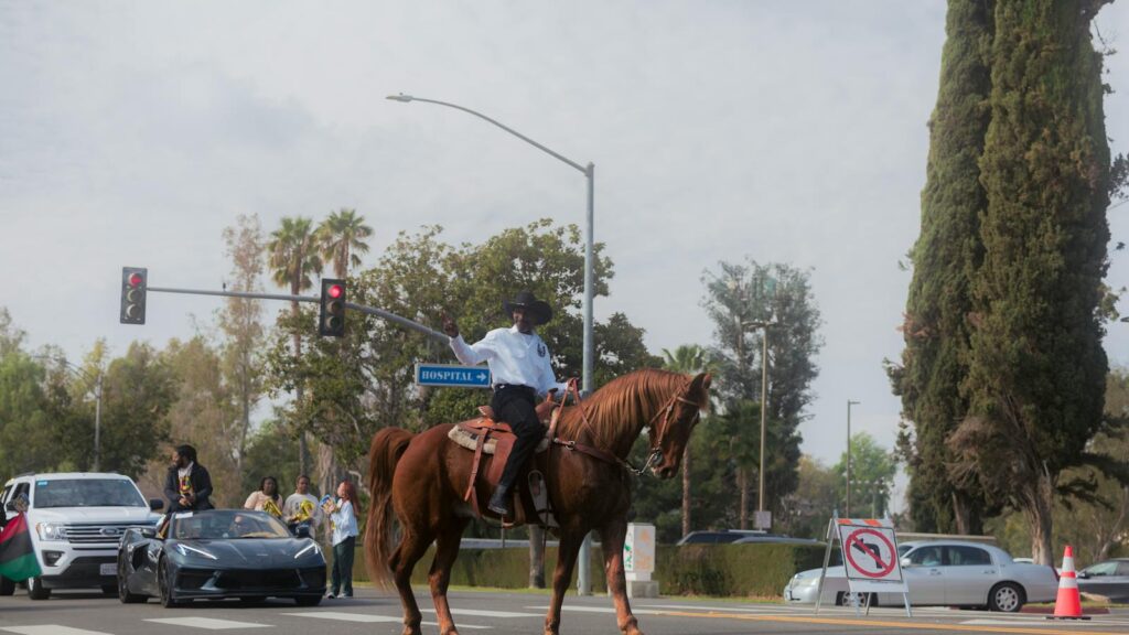 A cowboy confidently rides a horse through a busy city intersection, showcasing urban equestrian culture.