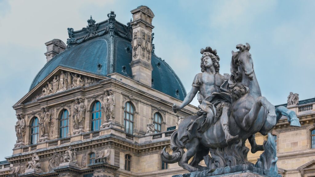 Intricate architectural details of the Louvre Museum in Paris, showcasing a historic statue.