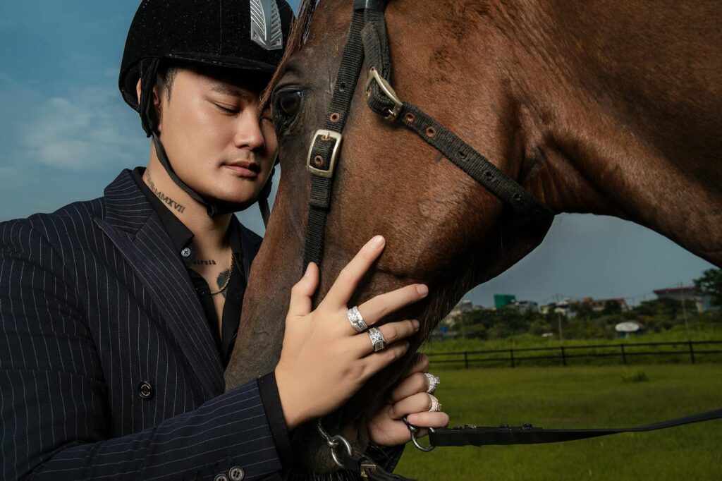 Young man in a helmet gently embracing a horse outdoors