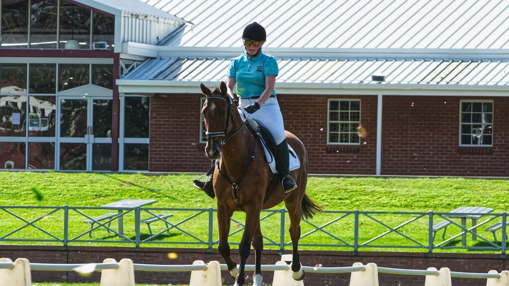 Equestrian rider in full gear performing dressage exercises outdoors beside a stable.
