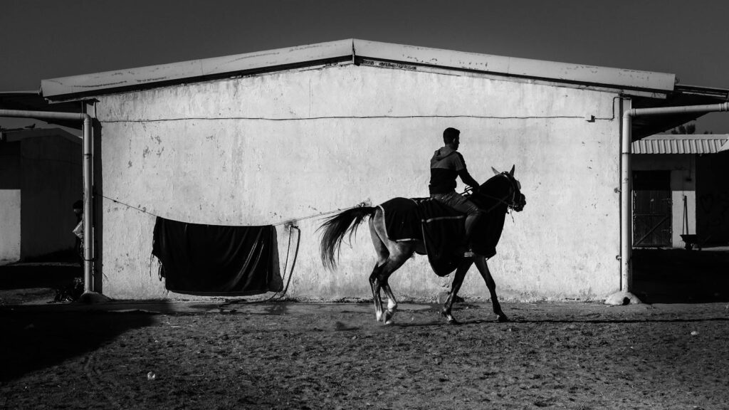 Silhouetted man on horse against barn in a dramatic black and white scene.