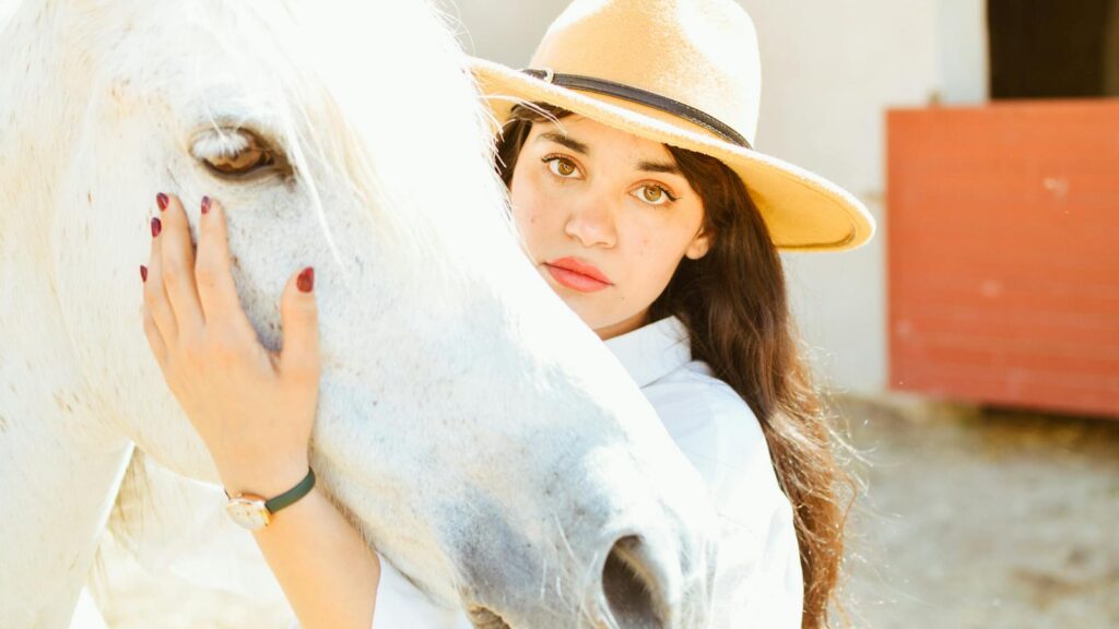 Woman in a hat lovingly caresses a white horse outdoors, creating a warm and serene moment.