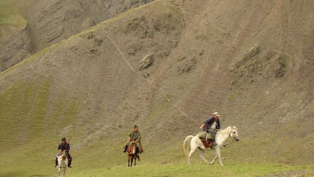 Three riders on horseback journey through a rugged mountain landscape.