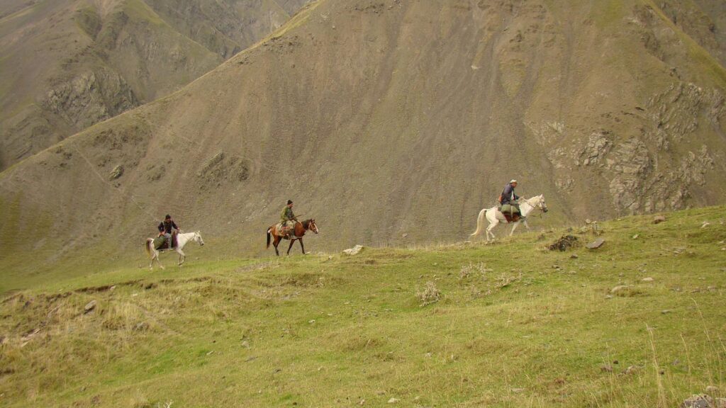 Three horse riders journey through rugged mountain landscape.