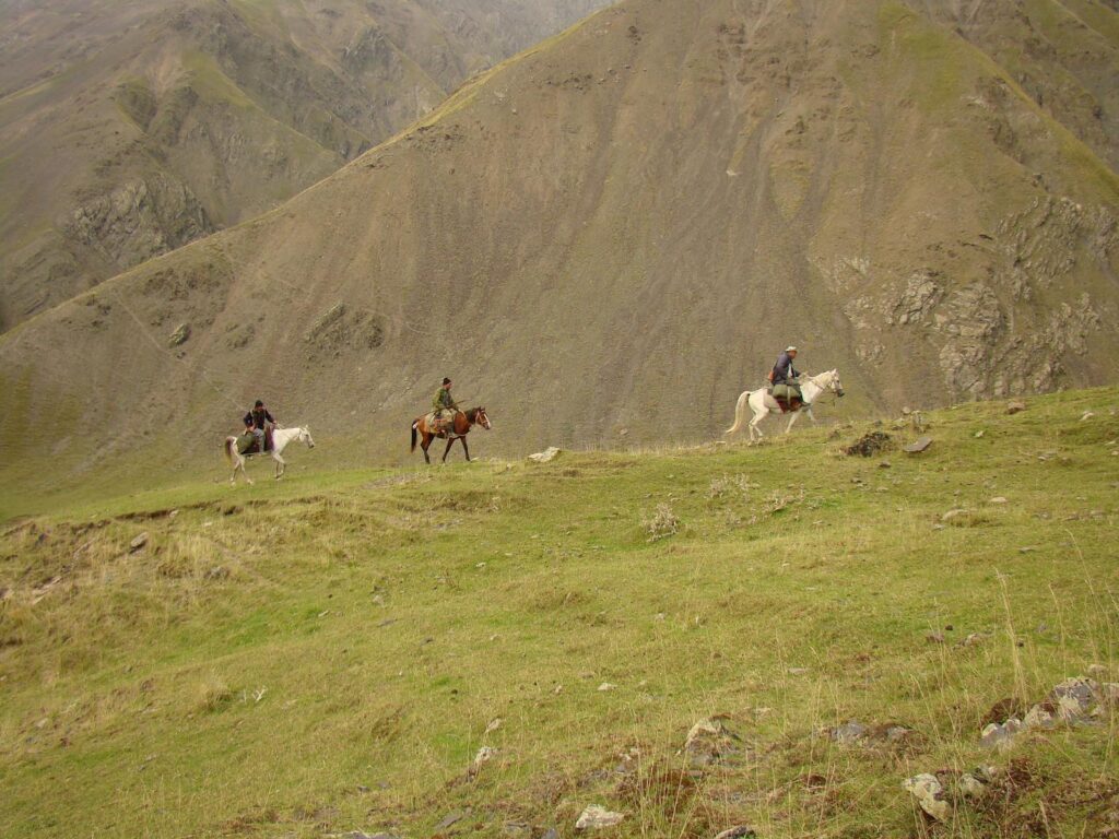 Three horse riders journey through rugged mountain landscape.
