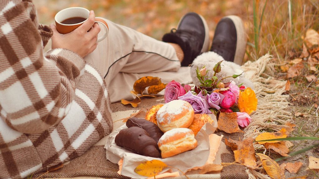 Cozy autumn picnic outdoors with coffee, pastries, and flowers on a blanket.