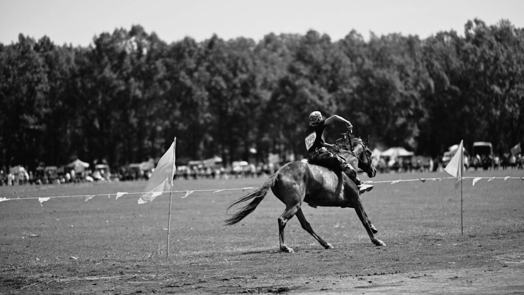 Black and white photo of a rider and horse in motion at an outdoor equestrian event.