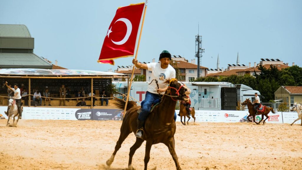 Man on horseback holding Turkish flag during an equestrian event.