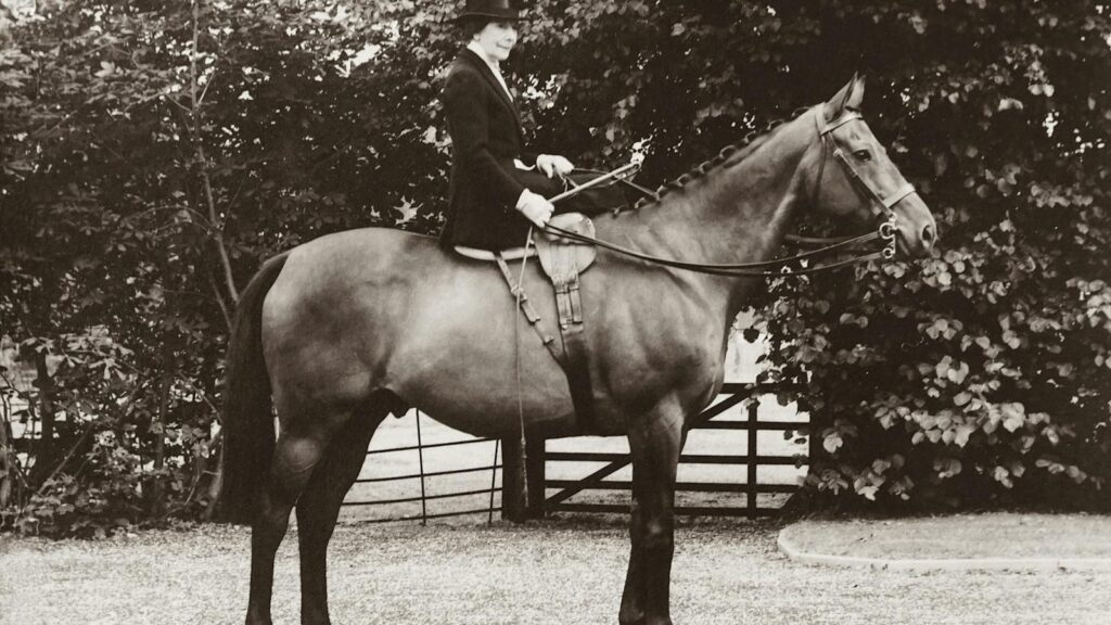 Classic sepia-toned photo of a woman in traditional riding attire on a horse.