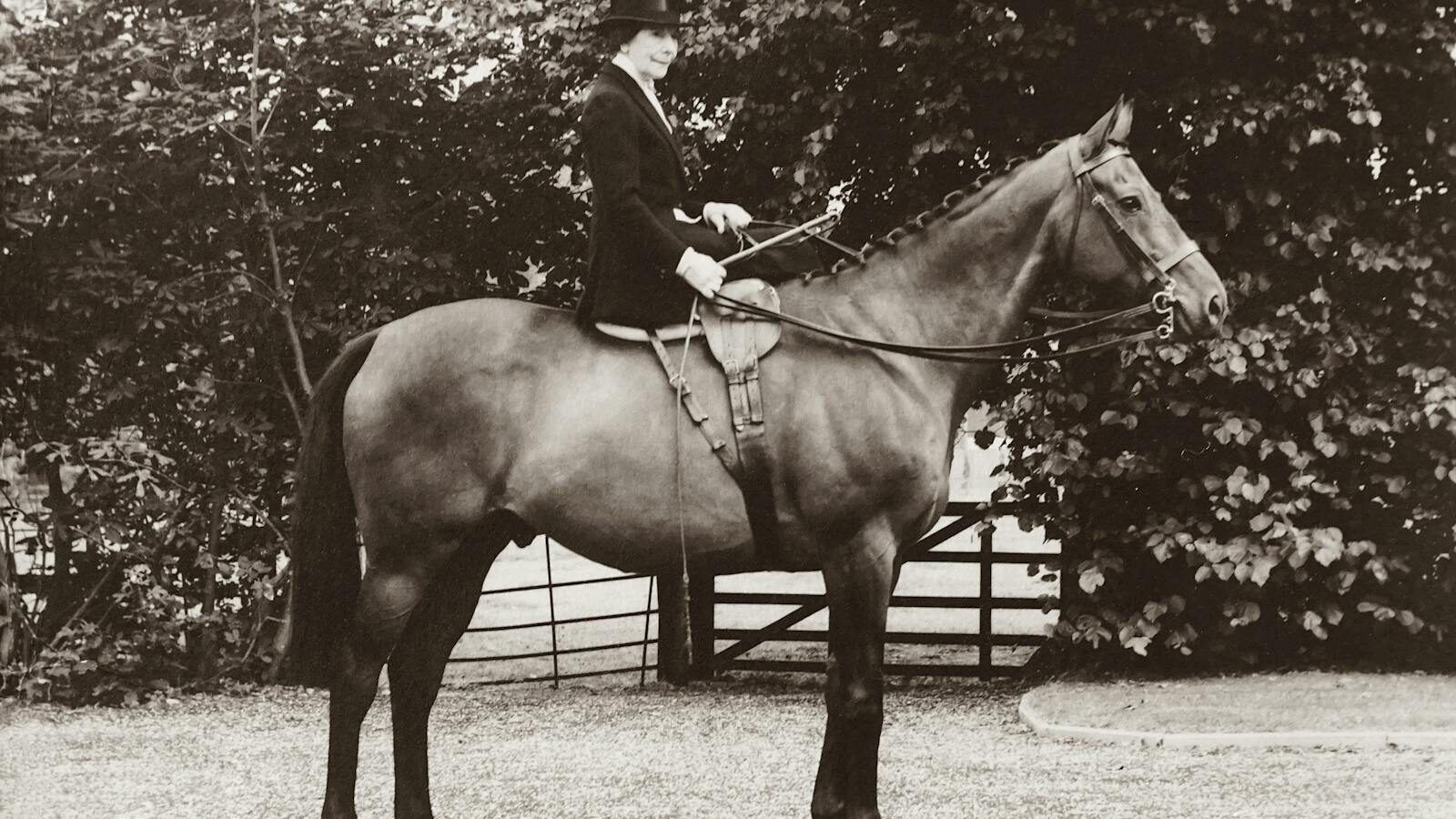 Classic sepia-toned photo of a woman in traditional riding attire on a horse.