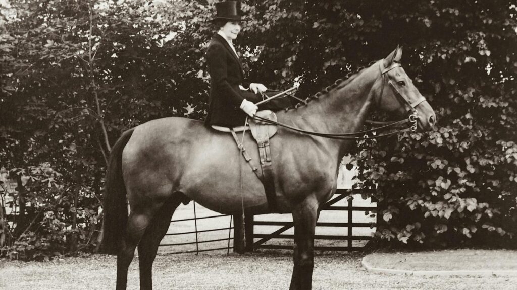 Classic sepia-toned photo of a woman in traditional riding attire on a horse.