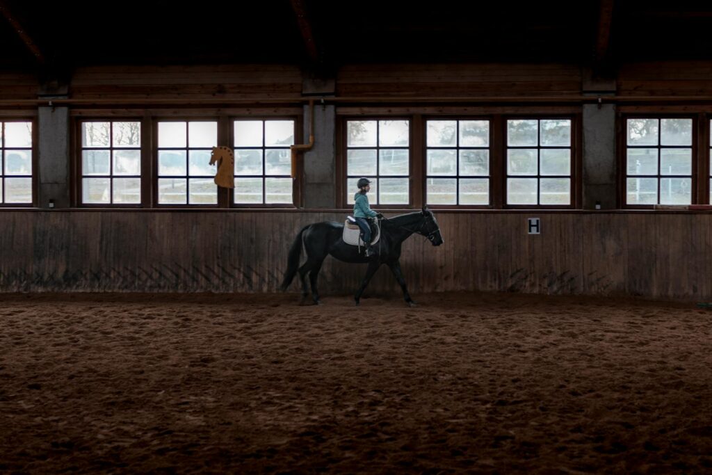 Girl riding a black horse indoors, showcasing equestrian training in a stable setting.
