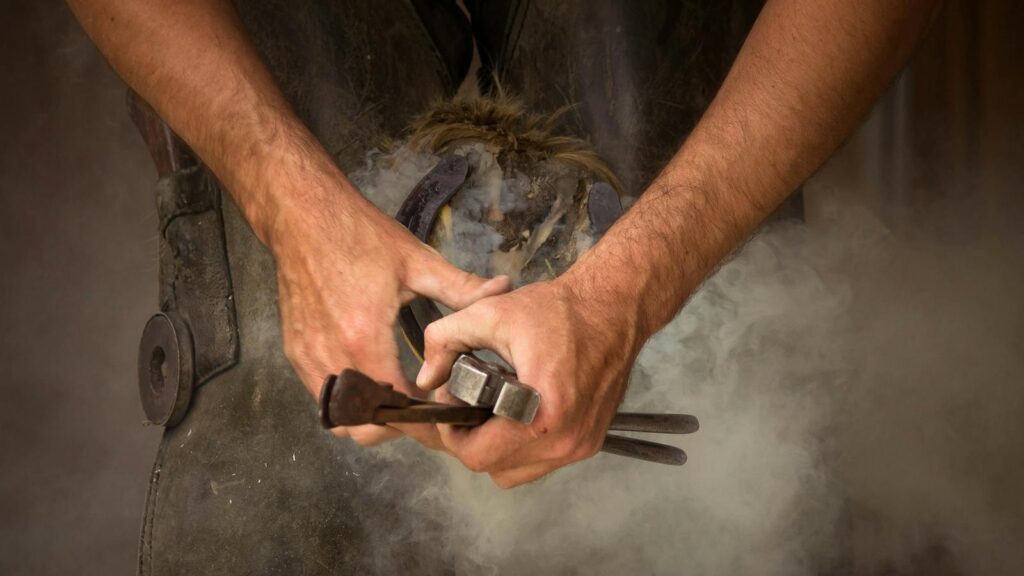 Close-up of a blacksmith shoeing a horse, showcasing the craftsmanship and smoke effect.