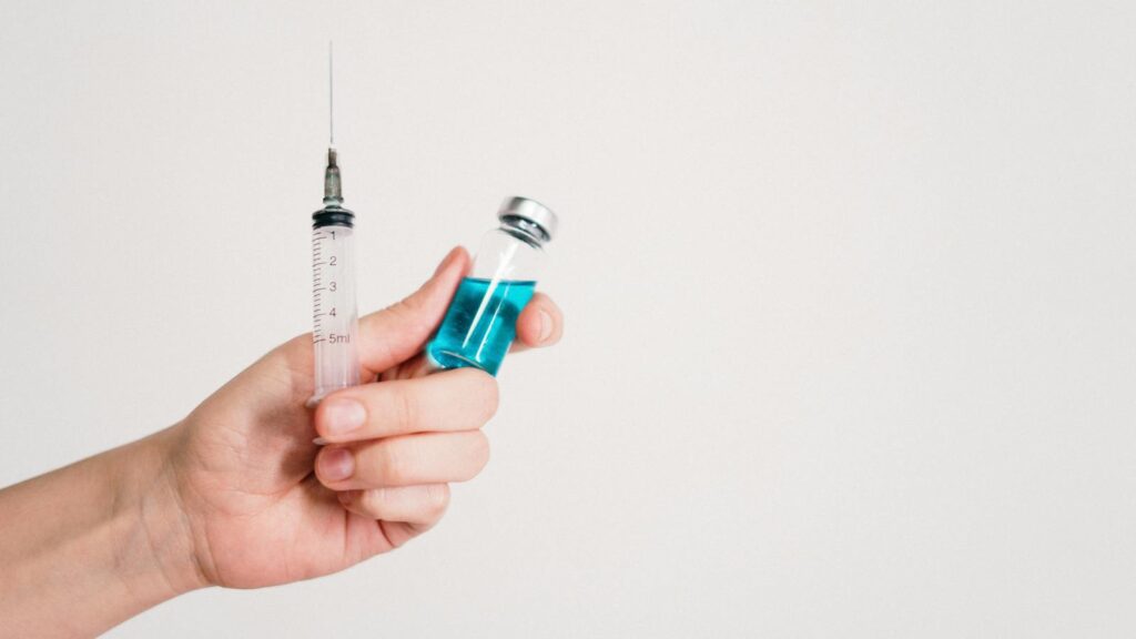 Hand holding a syringe and vaccine vial on a white background, symbolizing healthcare and immunization.