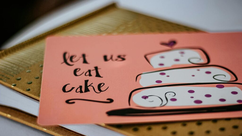 A vibrant greeting card with a cake design and message 'let us eat cake' on a table.