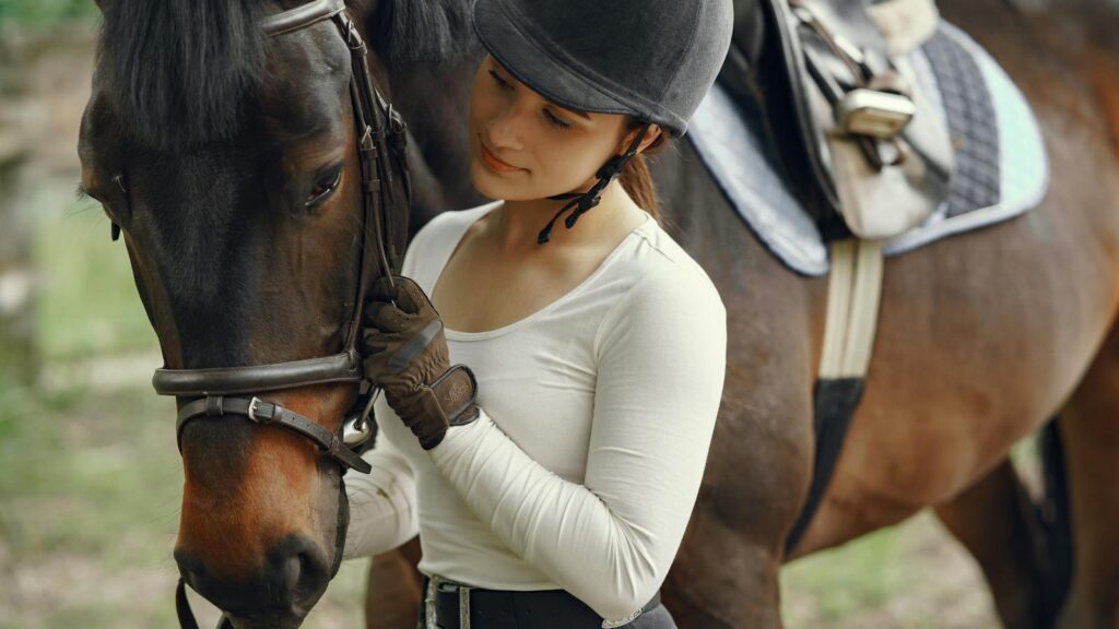 A young woman in equestrian gear affectionately holds a horse outdoors.