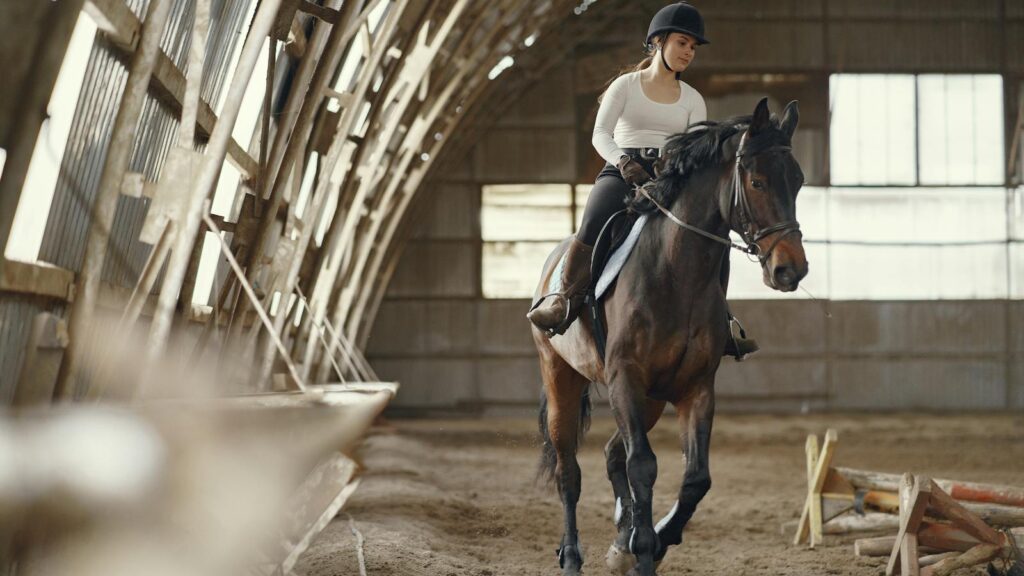 Woman practicing horseback riding indoors, focusing on equestrian skills.