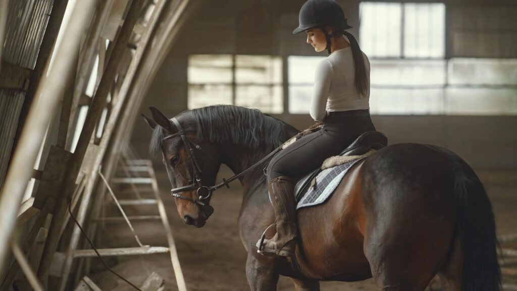 A young woman riding a horse indoors, dressed in equestrian attire, showcasing concentration and skill.