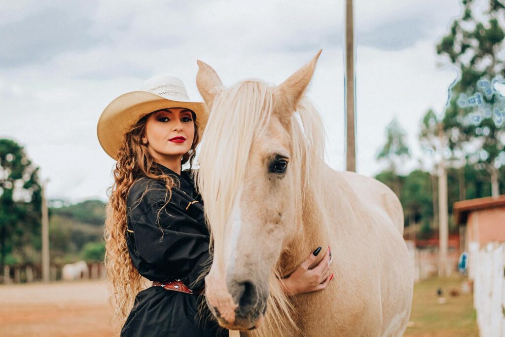 Woman in cowboy hat embraces a perlino horse