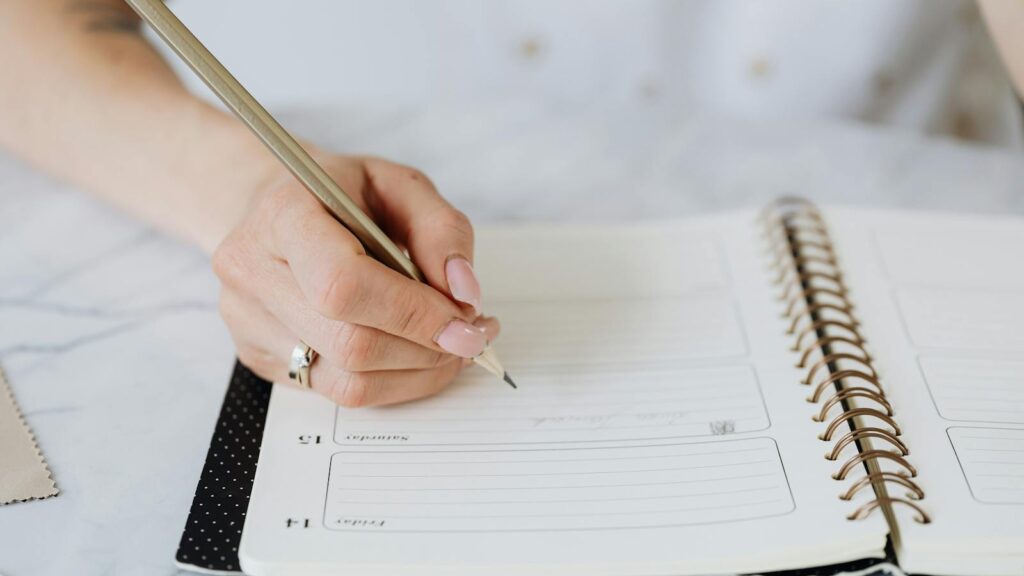 Close-up of a woman's hand writing in a spiral notebook on a marble desk.