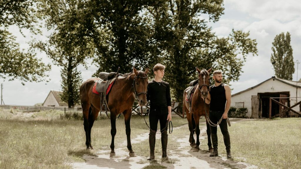 Two men with horses at a rustic stable, showcasing equestrian lifestyle.
