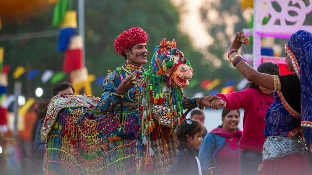 Vibrant celebration with a traditionally dressed man and ornate horse costume at an Indian festival.