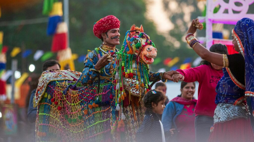 Vibrant celebration with a traditionally dressed man and ornate horse costume at an Indian festival.